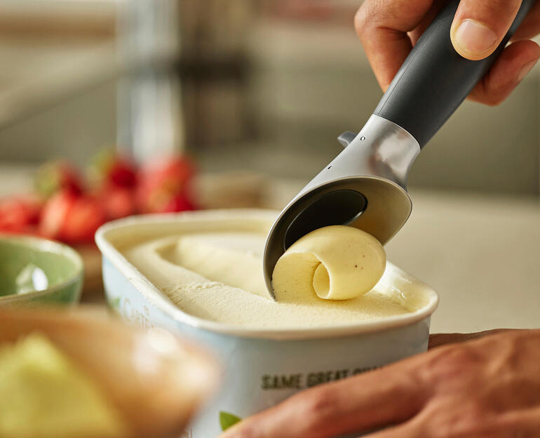 Gaat zelfs moeiteloos door hard bevroren ijs en sorbets heen. Hand die ijs uit een container met ijs schept met een lepel.