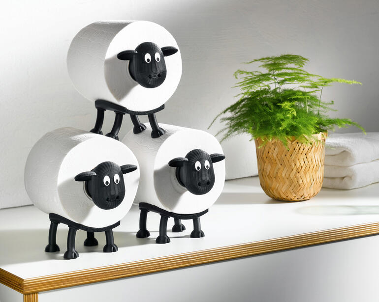Drie toiletpapierhouders in de vorm van schapen op een tafel.