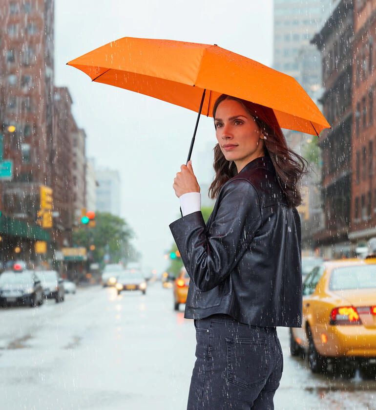 Vrouw houdt een oranje taschenscherm in de regen, staand op de straat.