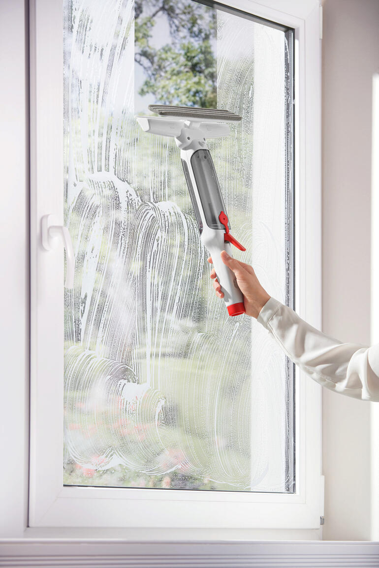 Persoon maakt raam schoon met 3-in-1 telescopische raamwisser, zeepoplossing op het glas.