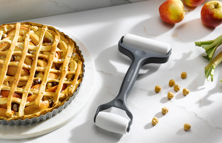 Dubbele deegroller staat naast een appeltaart op een keukentafel.