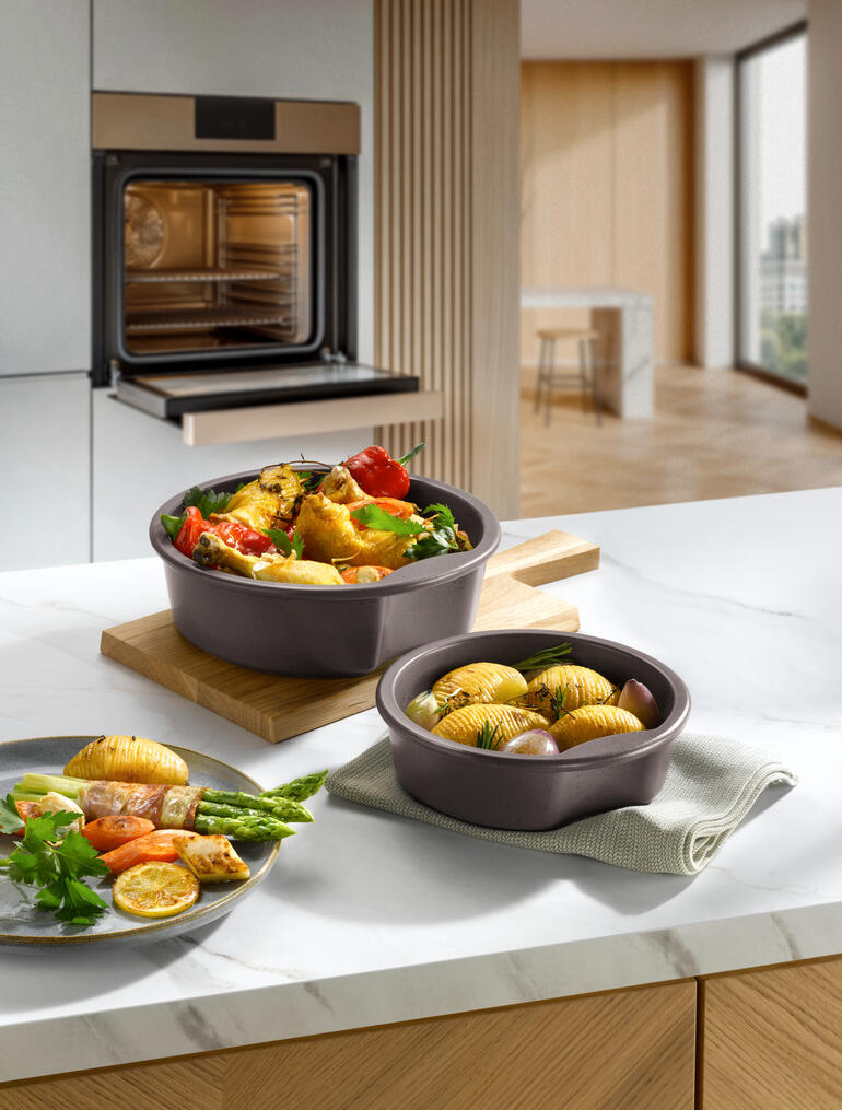Twee keltenpotten met groenten en aardappelen op een houten bord in een moderne keuken.