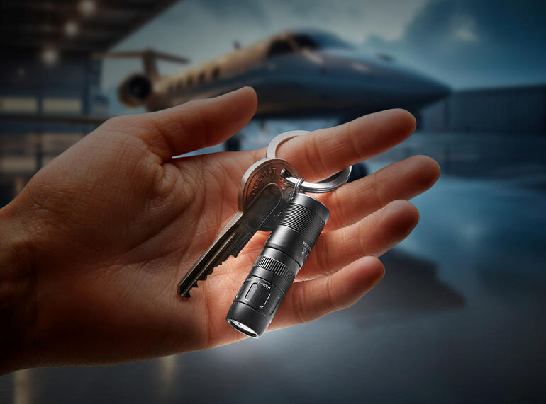 Hand houdt magnetische mini-zaklamp met sleutelring vast, licht straalt in het donker.