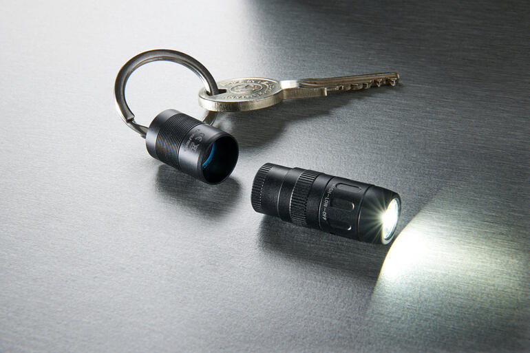 Gewoon van de sleutelring trekken en het licht gaat automatisch aan. Magnetische mini-zaklamp en sleutel op glanzend oppervlak, lamp straalt licht.