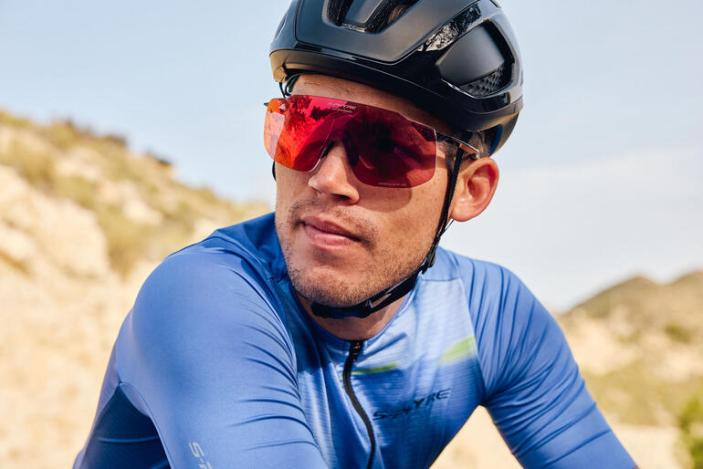 Fietser met rode sportzonnebril en zwarte helm op een pad.