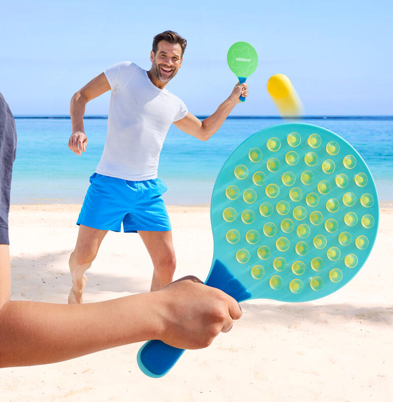 Man speelt op het strand met een ovale paddle en raakt de bal.