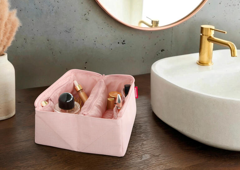 Open roze 2-in-1 reisnecessaire met verzorgingsproducten op een houten tafel
