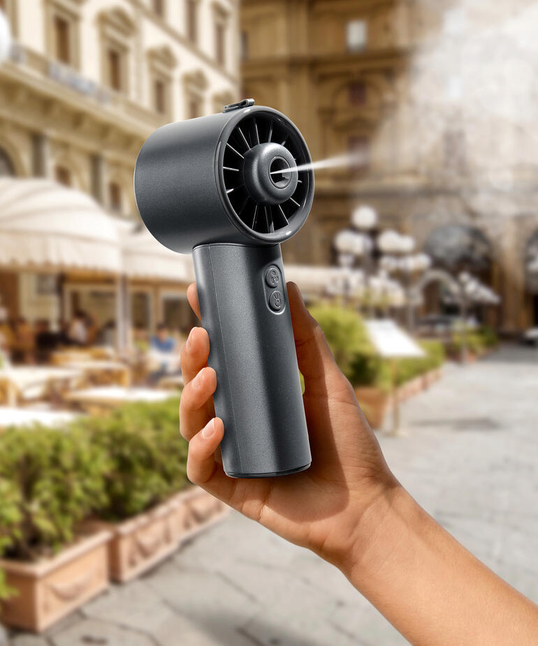 Hand houdt een Hydro-Mini-ventilator in een stad, met historische gebouwen op de achtergrond.