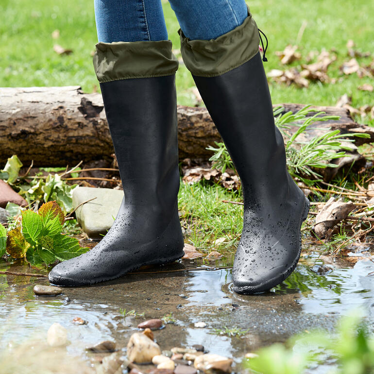 Zwarte rubberlaarzen met omgeslagen bovenkant, staan aan de rand van een waterloop.