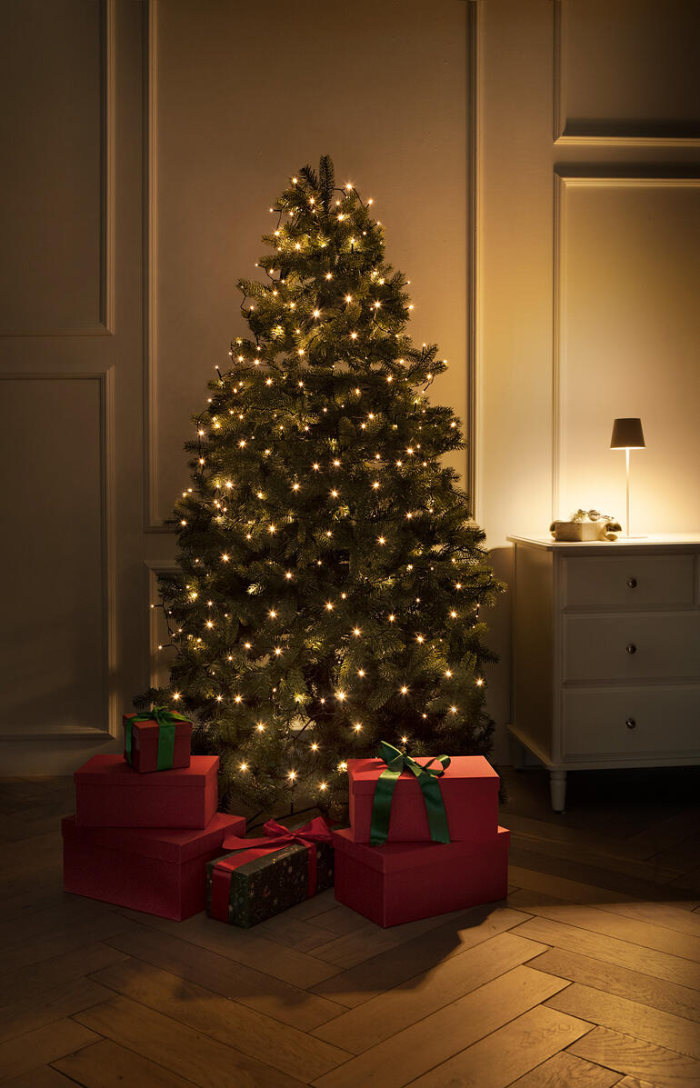Verlichte kerstboom met cadeaus en warm licht in een elegante ruimte.