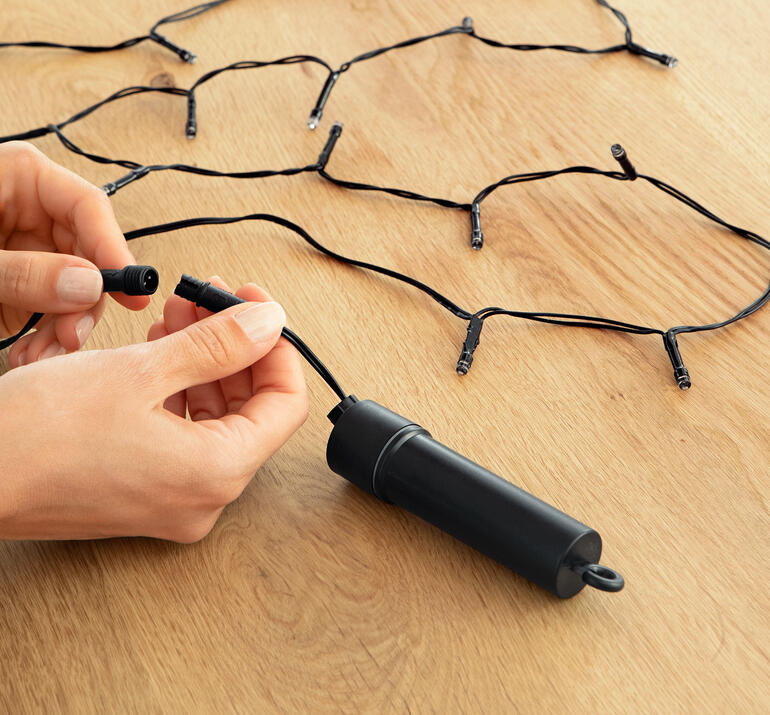 Persoon sluit de lichtslinger aan op een houten tafel.