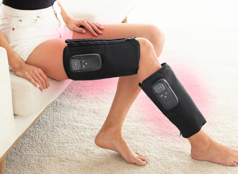 Vrouw met een compressiemassageapparaat op haar benen terwijl ze zit.