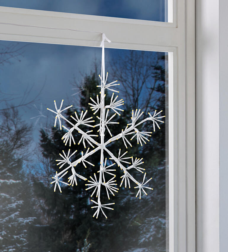 LED sneeuwvlok hangt aan het raam met uitzicht op de tuin.