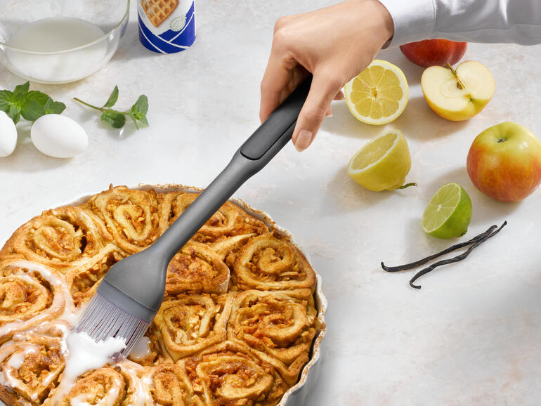 Hand met een bakborstel die een warme kaneeltaart aanbrengt.