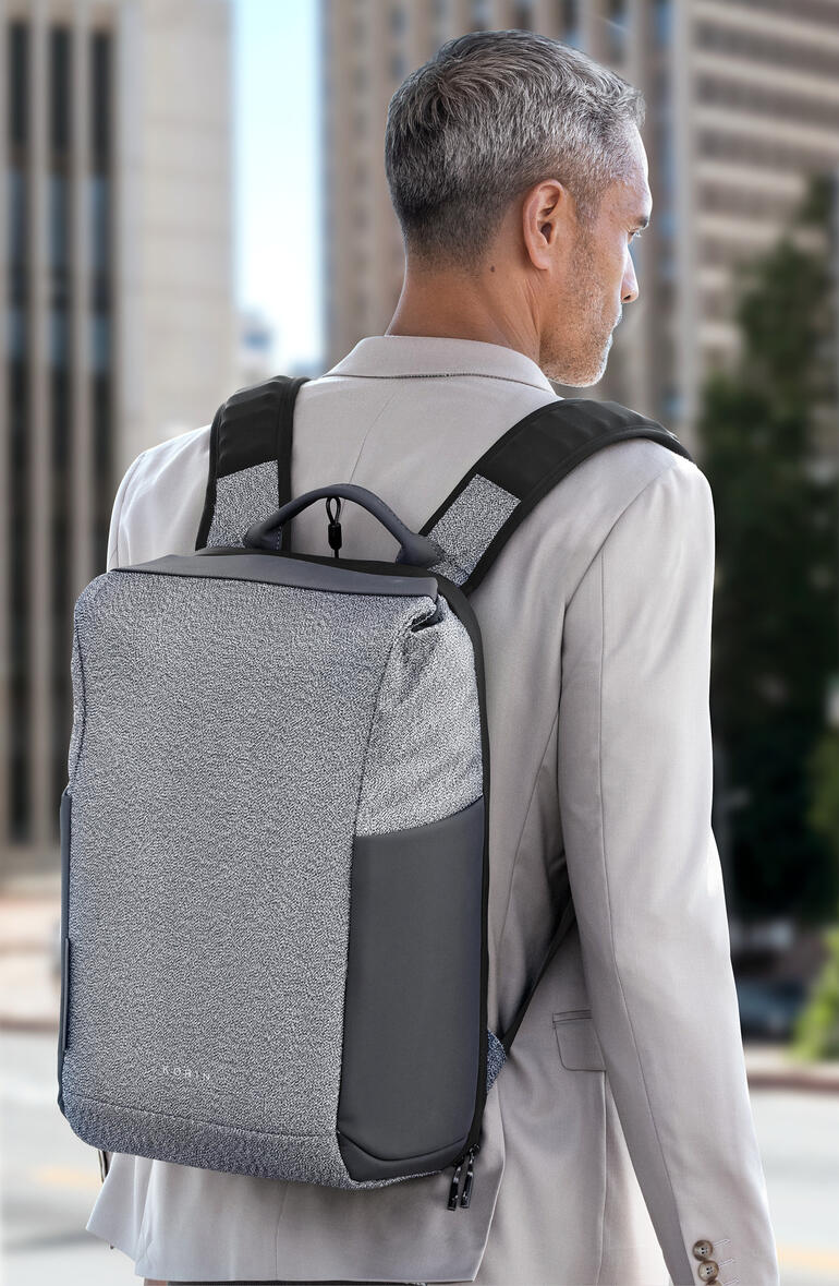 Man met grijze anti-diefstal rugzak op de rug voor een stedelijke achtergrond.