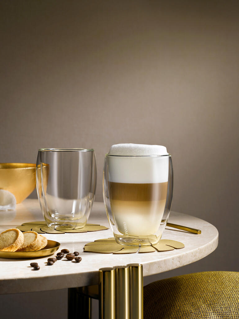 Twee premium thermobekers op tafel, één met schuimige drank en één leeg.