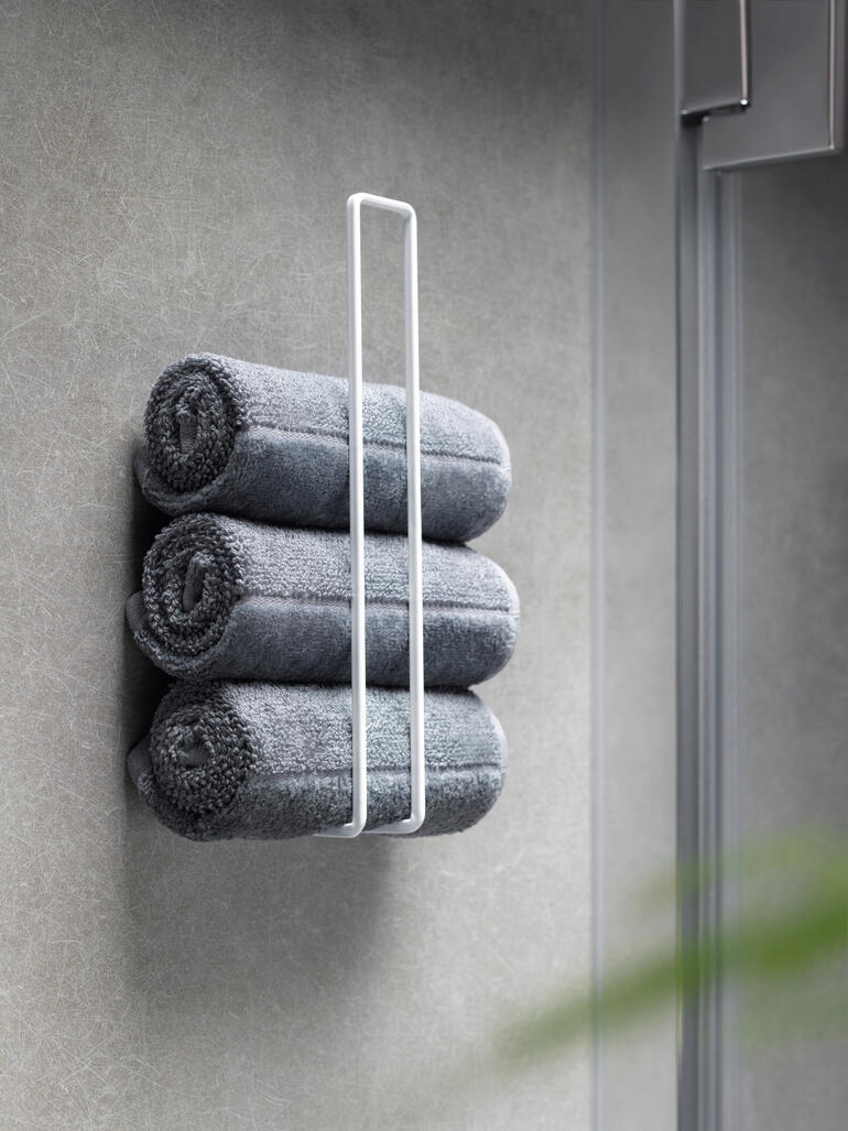 Drie grijze handdoeken netjes gestapeld in een witte design toiletrolhouder.
