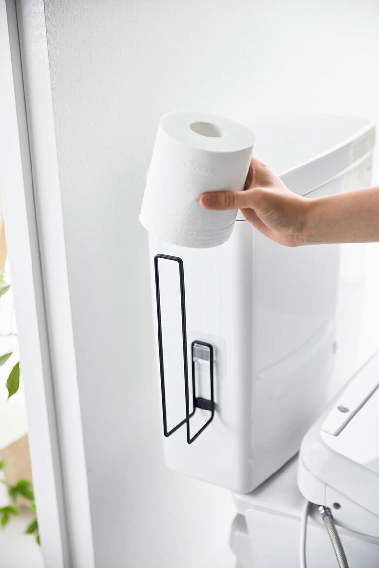Hand houdt een toiletrol aan een witte design toiletrolhouder.