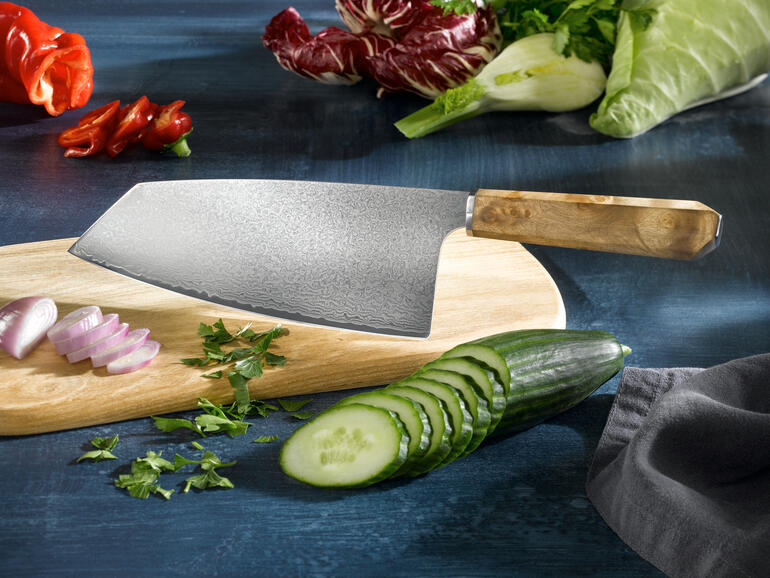 Damast Nakiri-mes op een houten plank, omringd door verse groenten.