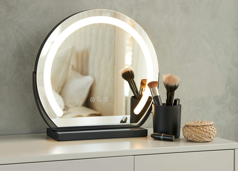 Ronde make-up spiegel met verlichting op een tafel, omringd door cosmetica accessoires.