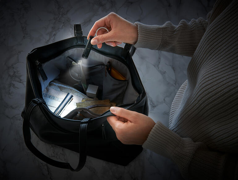 Twee handen houden een slimme micro-zaklamp in een tas