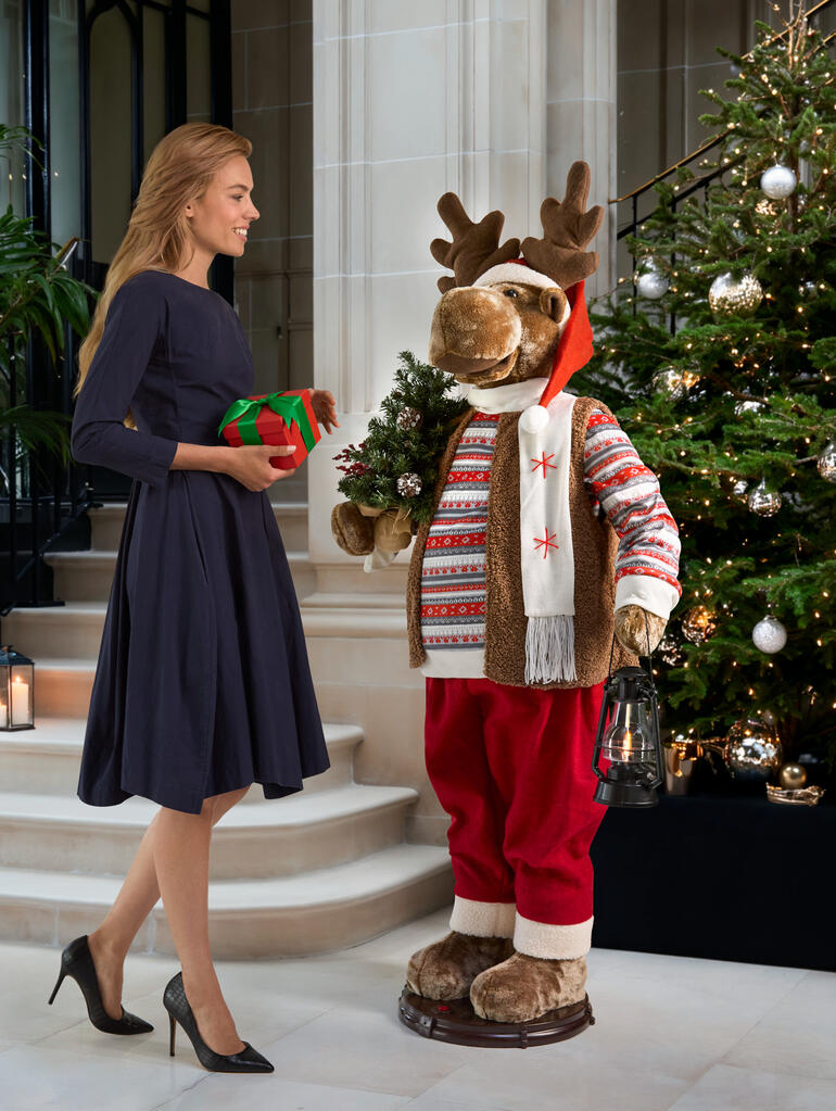 Dansende eland in feestelijke kleding, met een cadeau in de hand voor een kerstboom.