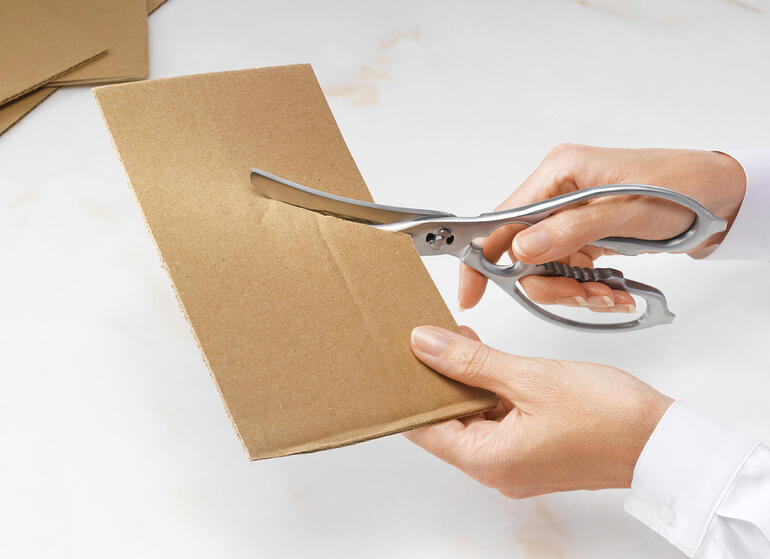 Tegelijkertijd ook een multifunctionele keukenschaar. Twee-in-een keuken- en gevogelschaar snijdt door bruin karton.