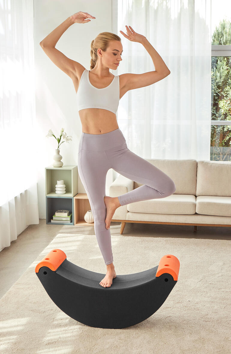 Vrouw staat op een 3-in-1 multifunctionele trainer en balanceert op één been.