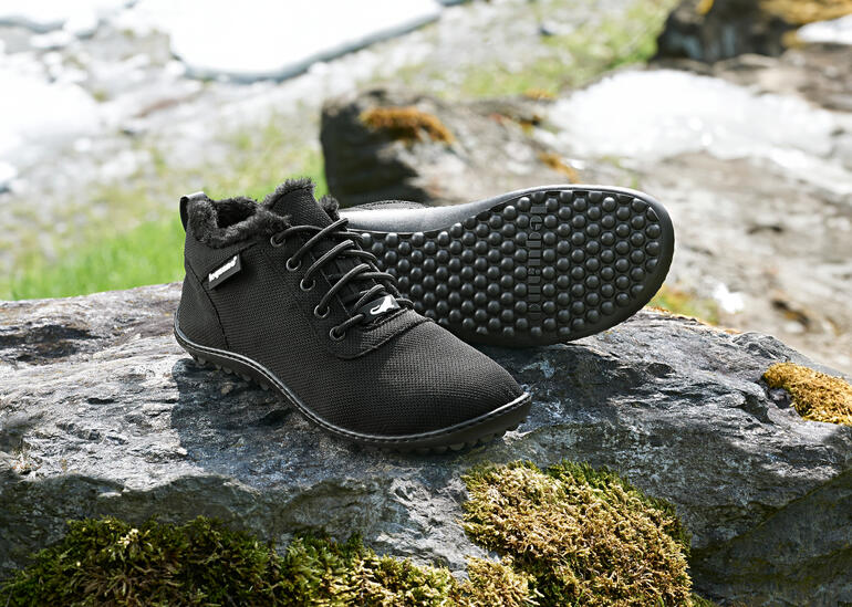 Zwarte winter sneakers op een steen met sneeuwresten op de achtergrond.