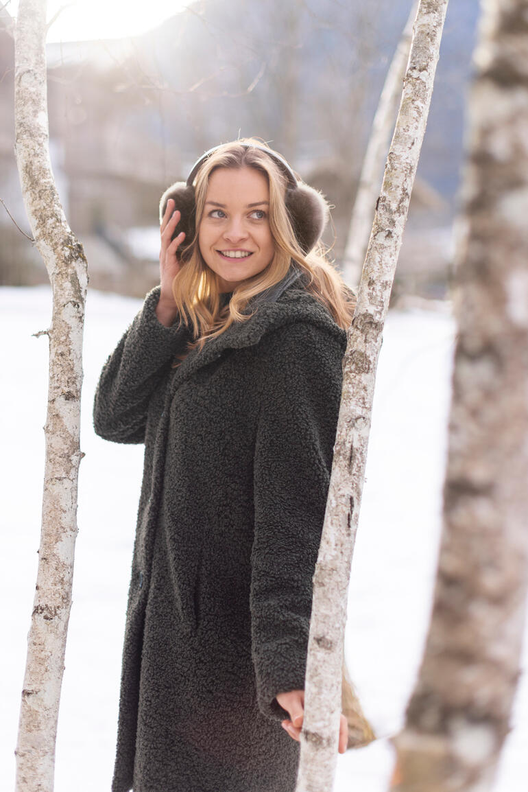 Vrouw met alpaca oorkappen staat voor berken in de sneeuw.