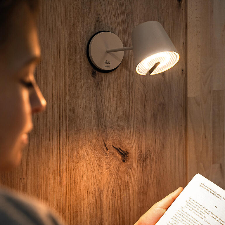 Zwarte wandlamp met helder licht boven een lezeres die een boek vasthoudt.