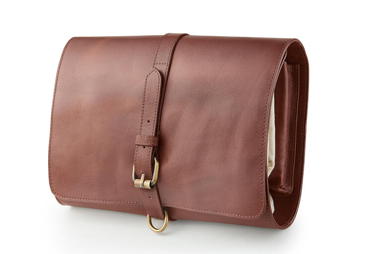 Dankzij de riemgesp blijft de opgerolde toilettas veilig gesloten. Buffellederen toilettas dicht met gesp, op een witte achtergrond.