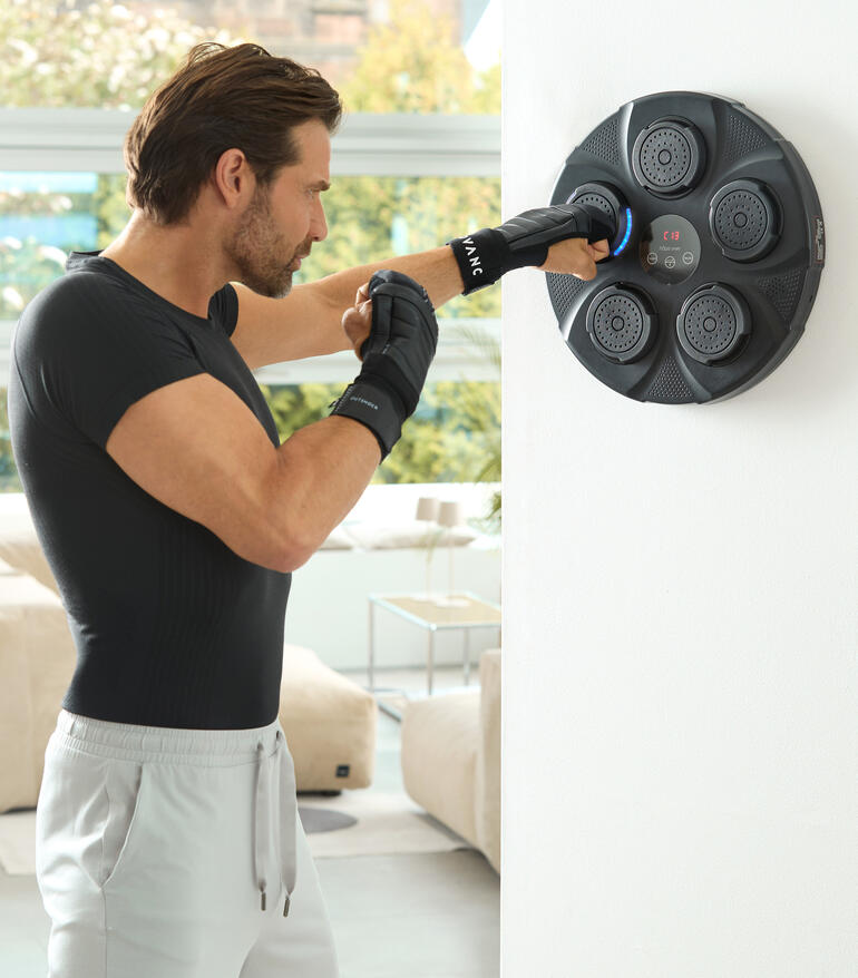 Man slaat met handen op wandbox trainer, fitnessruimte met heldere ramen op de achtergrond.