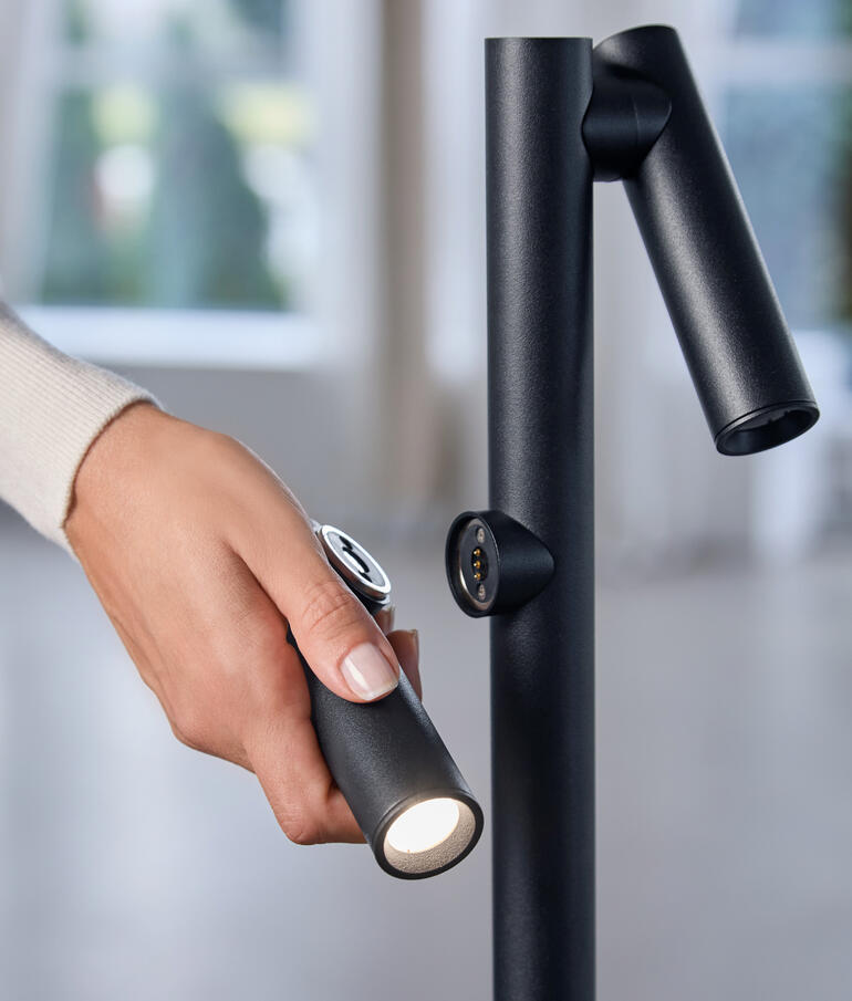 Hand grijpt naar de zaklamp van de vloerlamp voor gerichte verlichting.