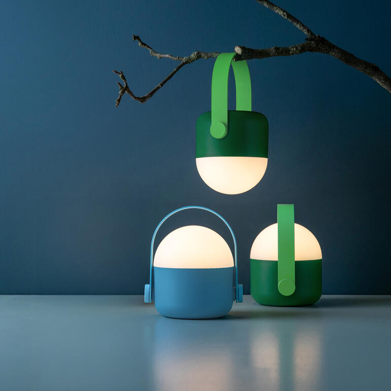 Drie mobiele acculampen in blauw en groen hangen aan een tak.