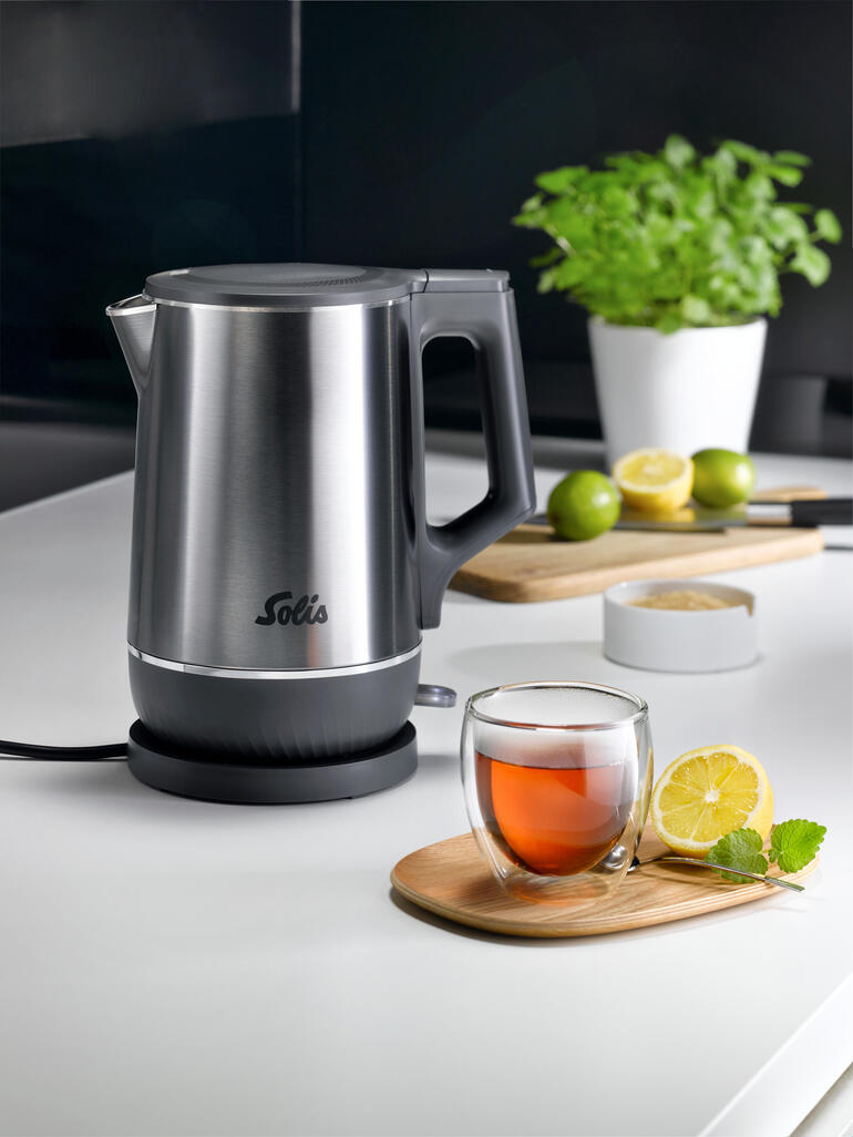 Dubbele waterkoker met roestvrijstalen afwerking en thee in glazen kom op tafel.