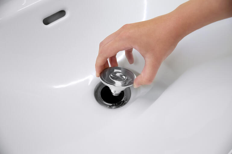 Hand die universele wastafelstop met afvoersieb in de gootsteen pakt.