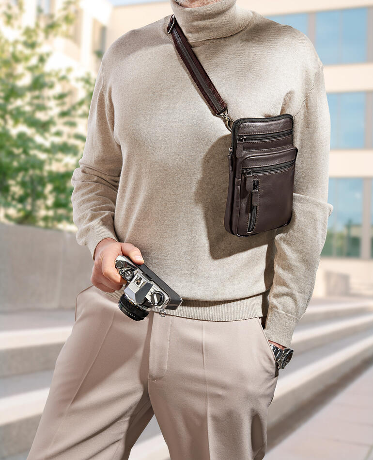 Man draagt een buffelleer heuptas over zijn schouder en houdt een camera vast.