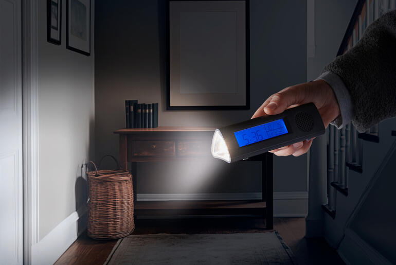 Hand houdt een radio-alarmklok met LED-zaklamp in een donkere kamer.