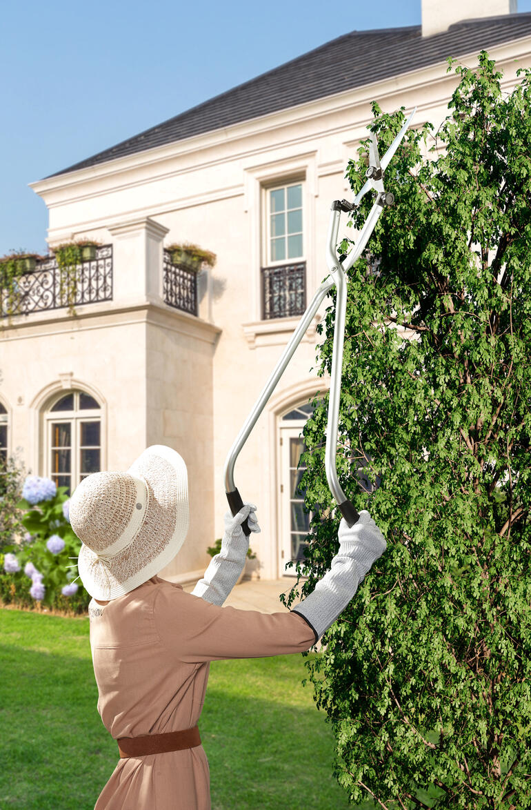 Vrouw snoeit met een multi-angle takkenschaar hoge planten in de tuin.