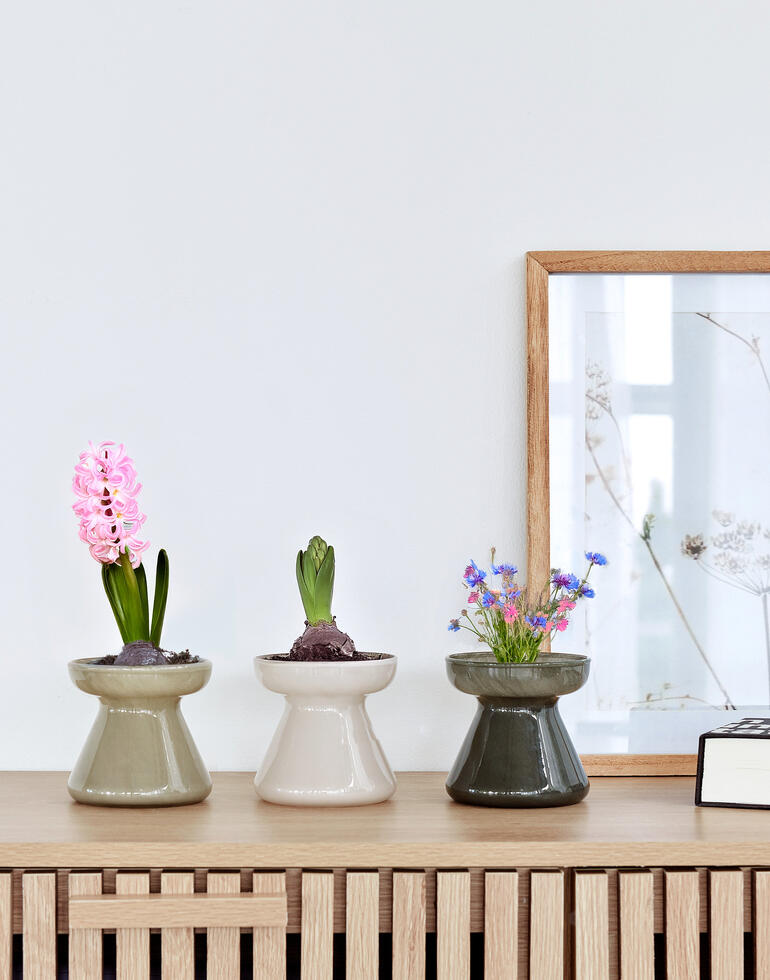 Drie decoratieve potten met bloemen in modern design op een rek.
