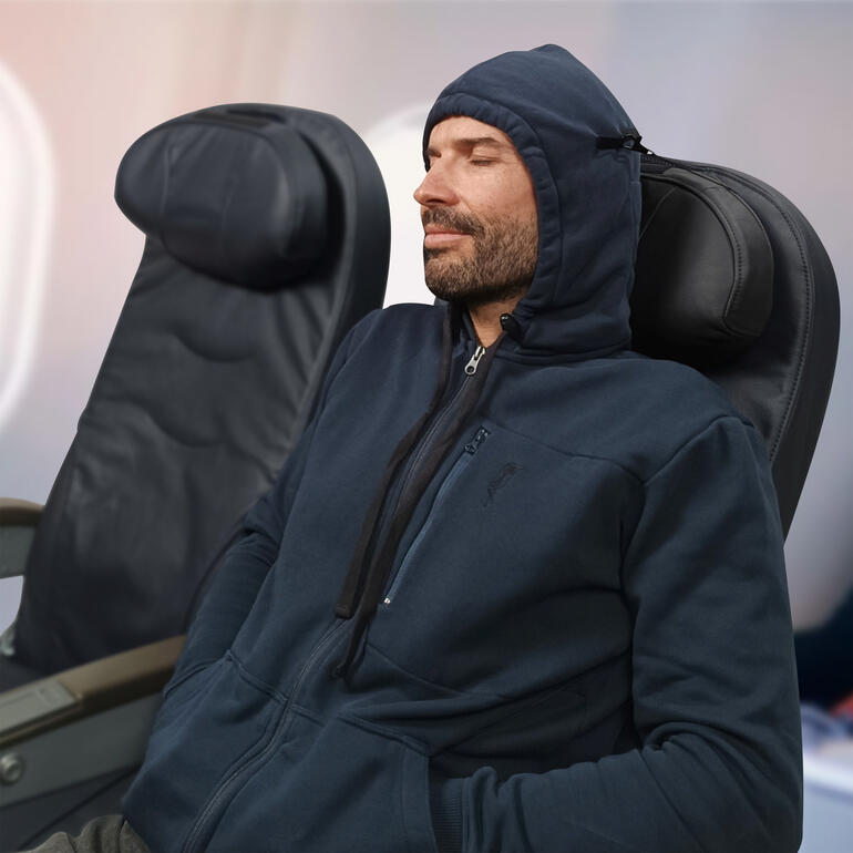 Man in reishoodie zit ontspannen in het vliegtuig met capuchon op.