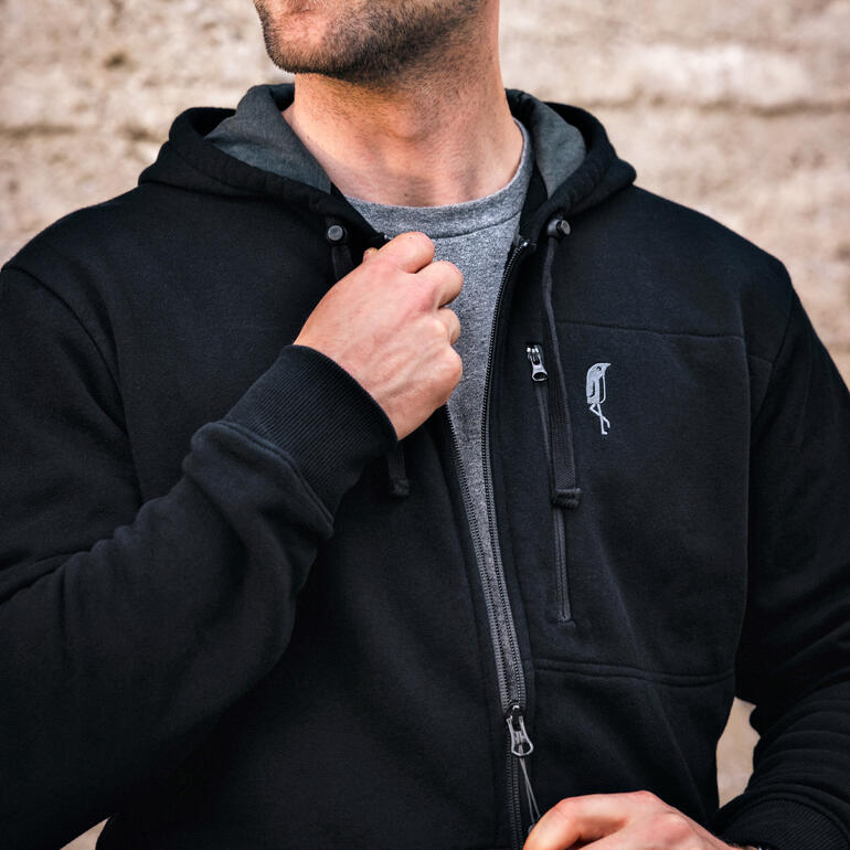 Man in zwarte hoodie sluit een rits en glimlacht lichtjes.