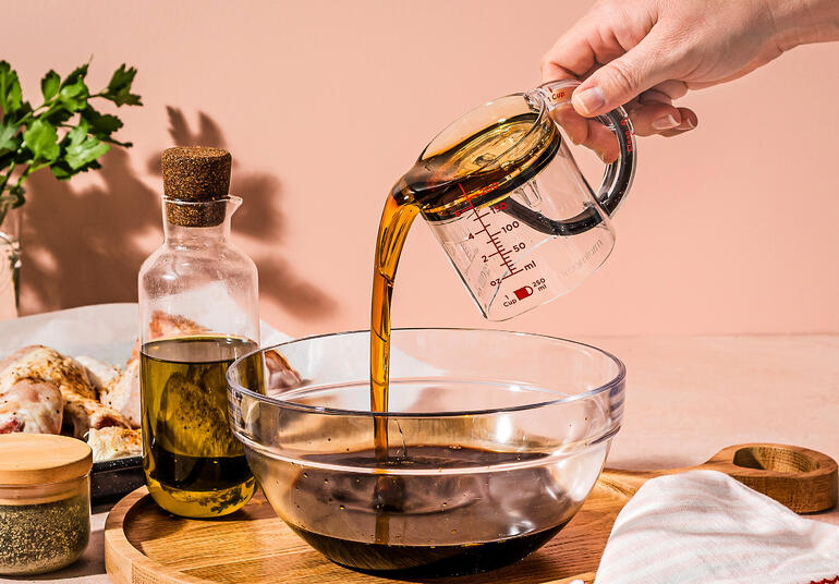 Persoon giet olie uit een maatbeker in een kom.