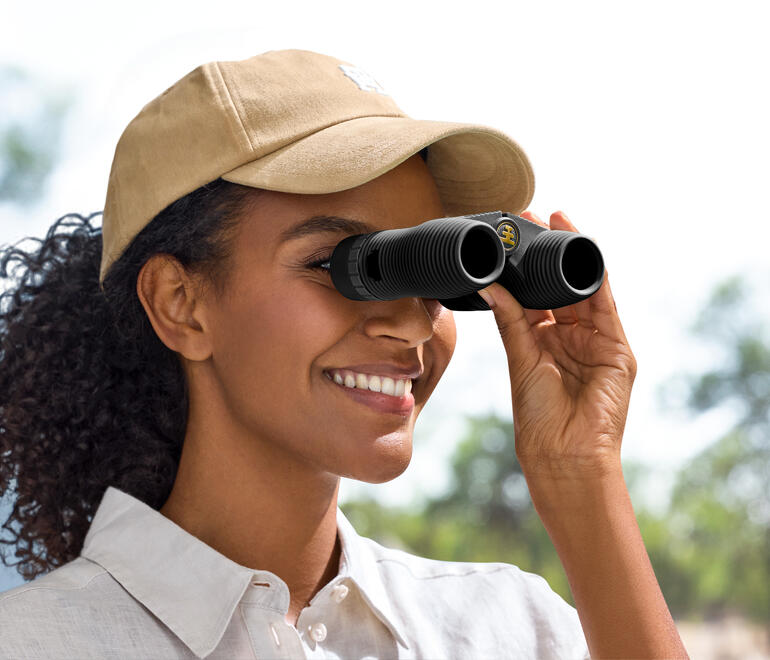 Vrouw kijkt door een compacte verrekijker in de natuur.