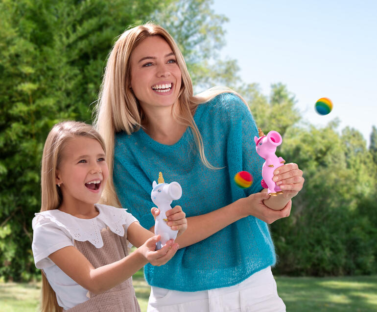 Vrouw en meisje lachen terwijl ze buiten met eenhoorn-ploppers spelen.