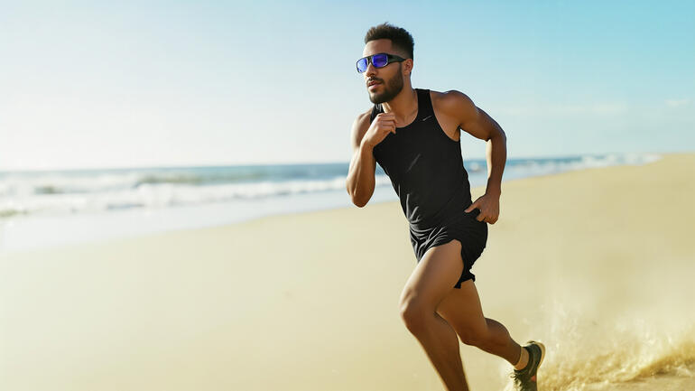 Man in sportkleding loopt op het strand met lichtglazen.