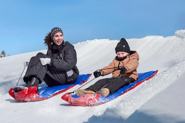 Vrouw en kind glijden van een sneeuwhelling met XL-sleetjes.
