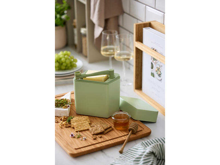 Kaas vershoudbox met snijder op een houten snijplank naast crackers en honing.