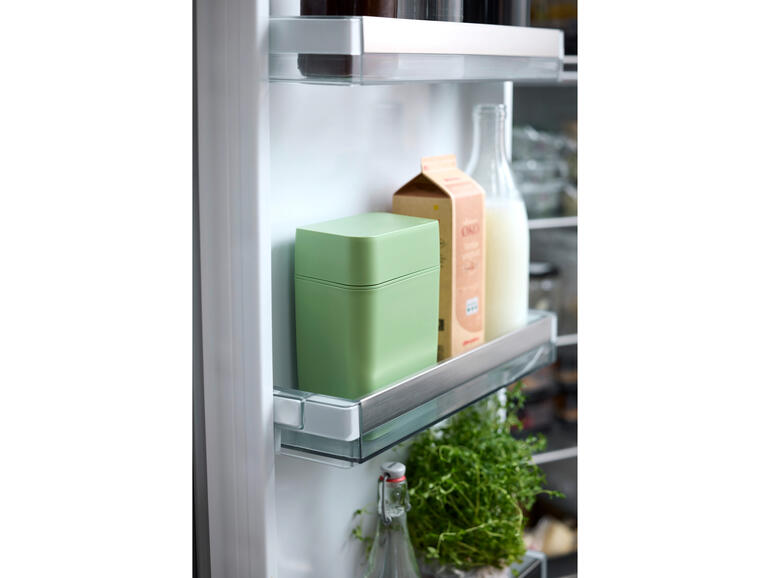 Kaas vershoudbox in de koelkast, omgeven door melk en kruiden.